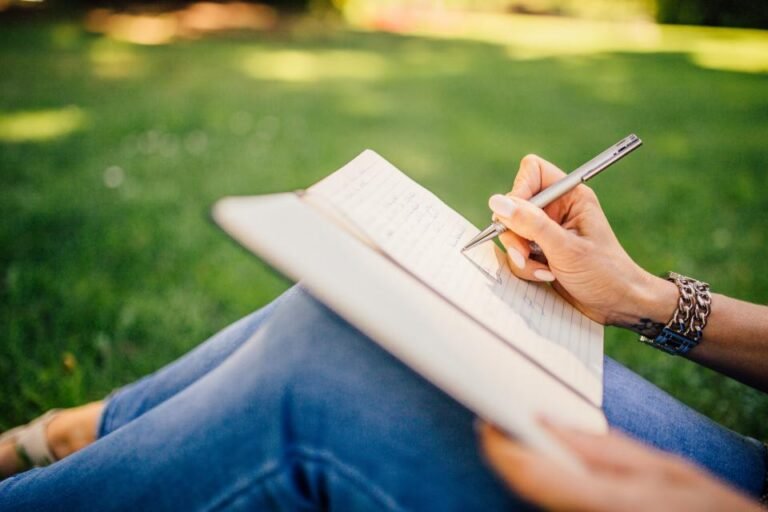 Personne écrivant au crayon dans un carnet, assise dans l’herbe